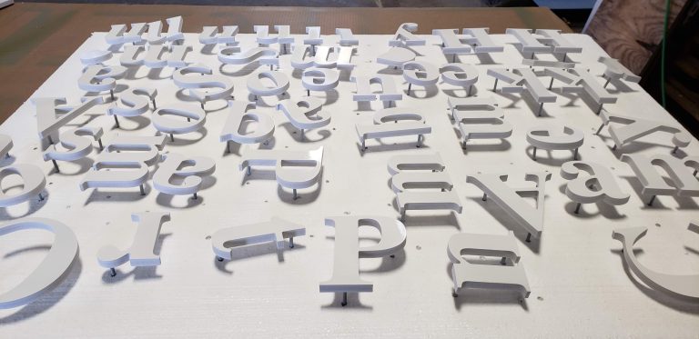Past dimensional-letter production: freshly painted white letters raised on studs above a finishing board.